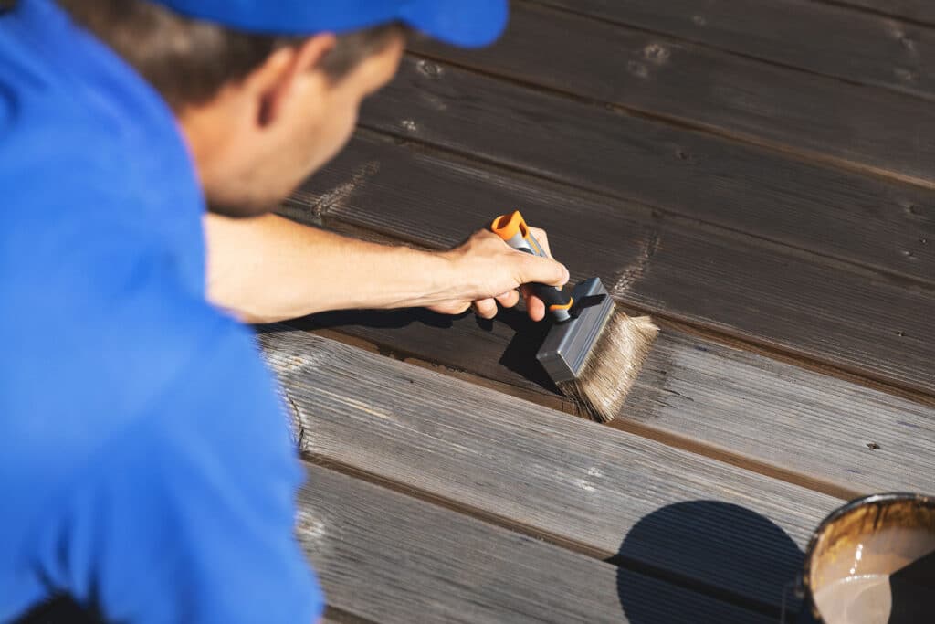man painting wooden terrace planks with wood protection oil